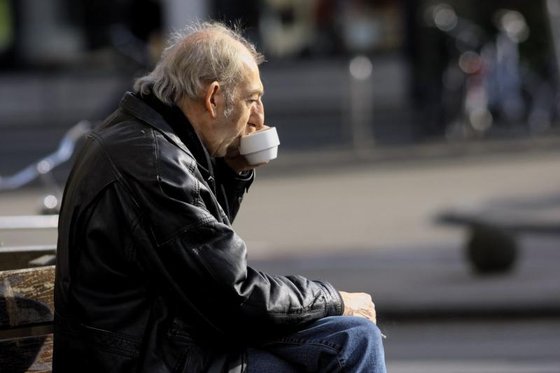 older man drinking tea on a park bench